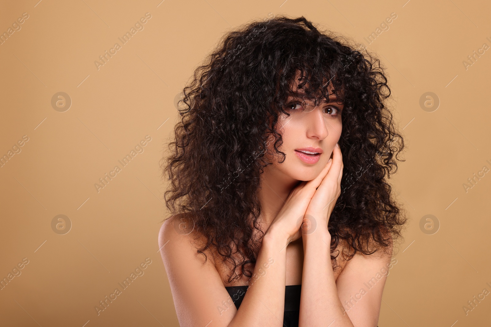 Photo of Beautiful young woman with long curly hair on beige background. Space for text