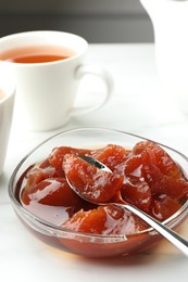 Quince jam in glass bowl served to tea on white table, closeup