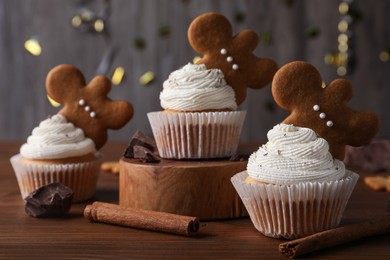 Tasty Christmas cupcakes with gingerbread man cookies on wooden table