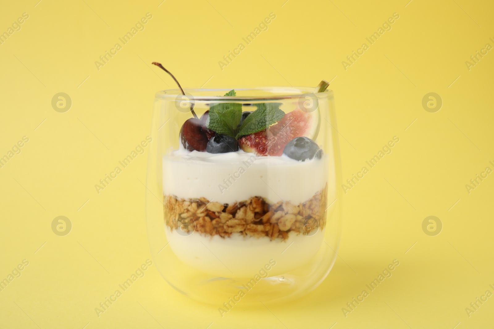 Photo of Glass with yogurt, berries and granola on yellow background