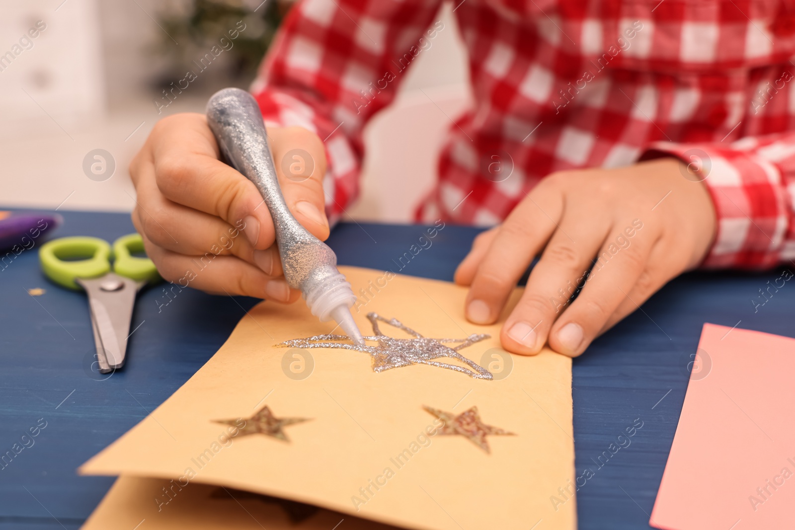 Photo of Little child making Christmas card at blue wooden table, closeup