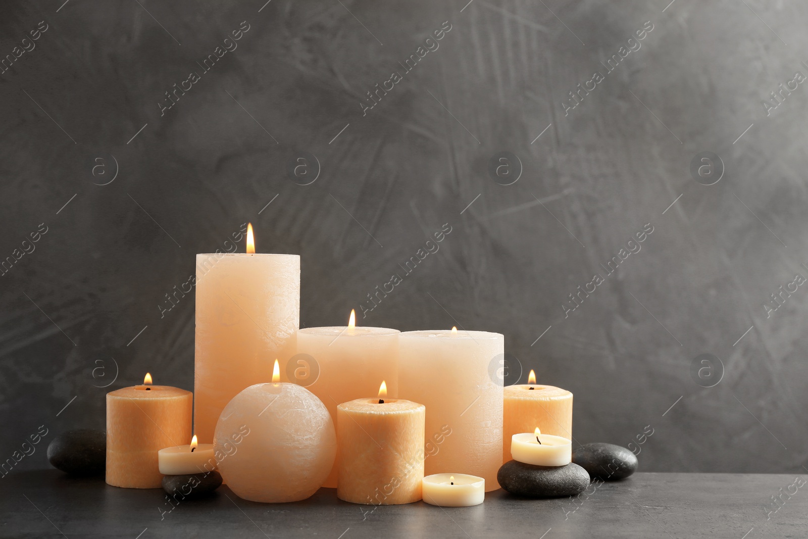 Photo of Beautiful composition with lit candles and spa stones on table. Space for text