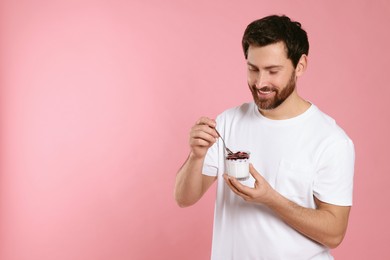 Photo of Handsome man with delicious yogurt and spoon on pink background. Space for text