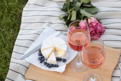 Photo of Glasses of delicious rose wine, flowers and food on picnic blanket outdoors