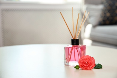 Photo of Aromatic reed air freshener and rose on table indoors