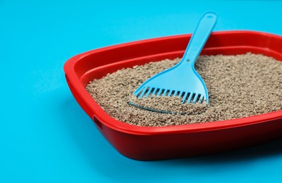 Cat litter tray with filler and scoop on light blue background, closeup
