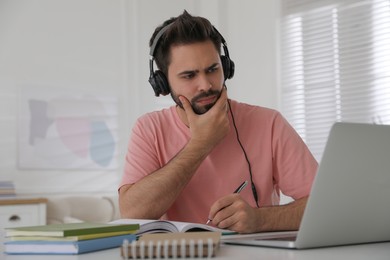 Confused young man watching webinar at table in room