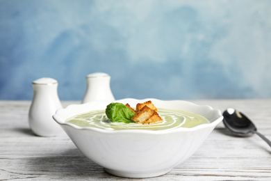 Photo of Delicious broccoli cream soup with croutons served on white wooden table. Space for text