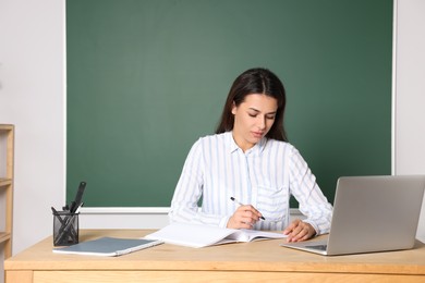Photo of Young teacher giving lesson at table in classroom