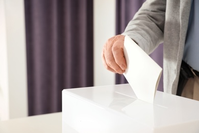 Elderly man putting ballot paper into box at polling station, closeup