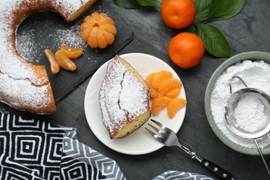 Photo of Piece of delicious homemade yogurt cake with powdered sugar and tangerines on gray table, flat lay
