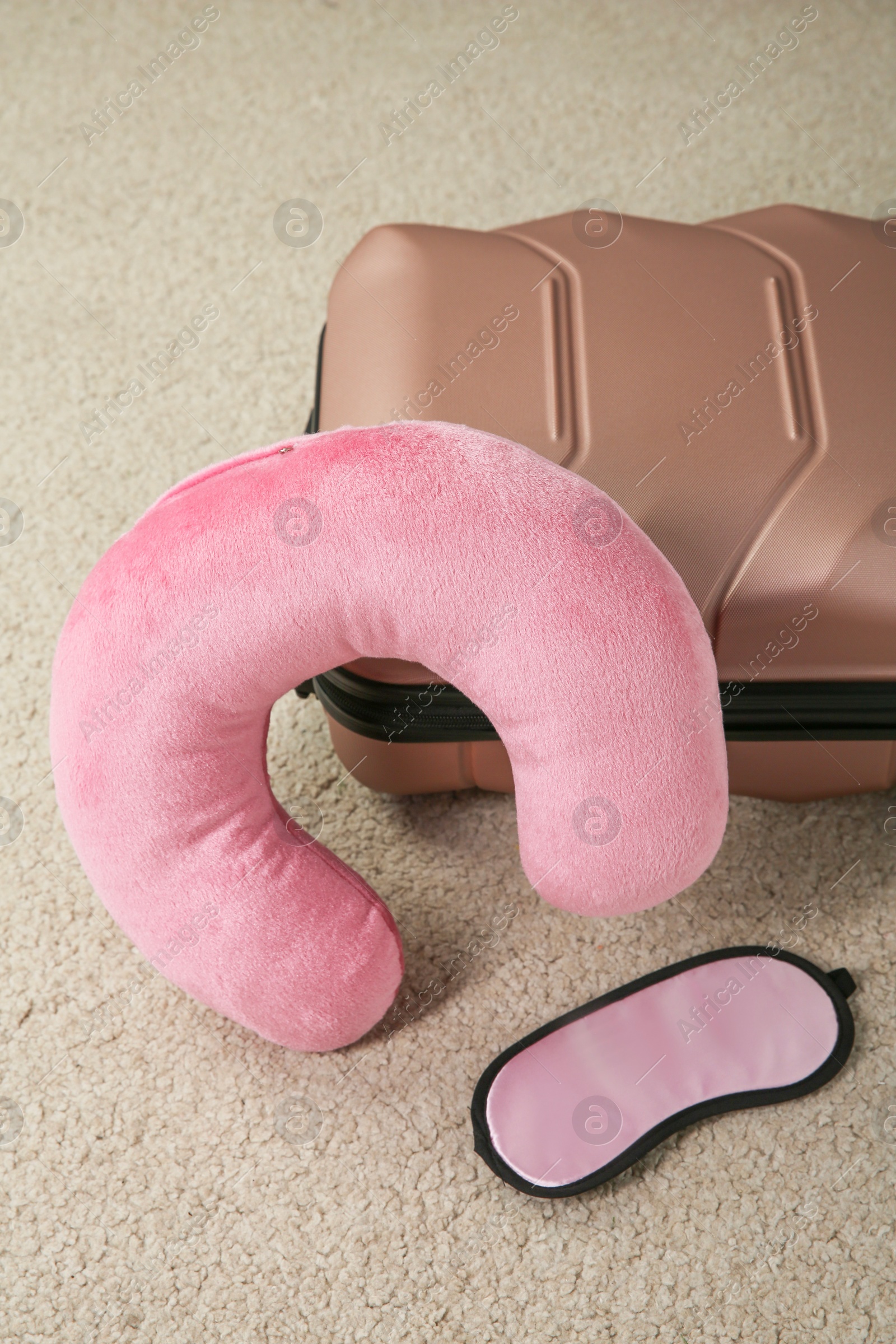 Photo of Pink travel pillow, suitcase and sleep mask on beige rug