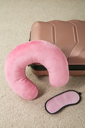 Photo of Pink travel pillow, suitcase and sleep mask on beige rug