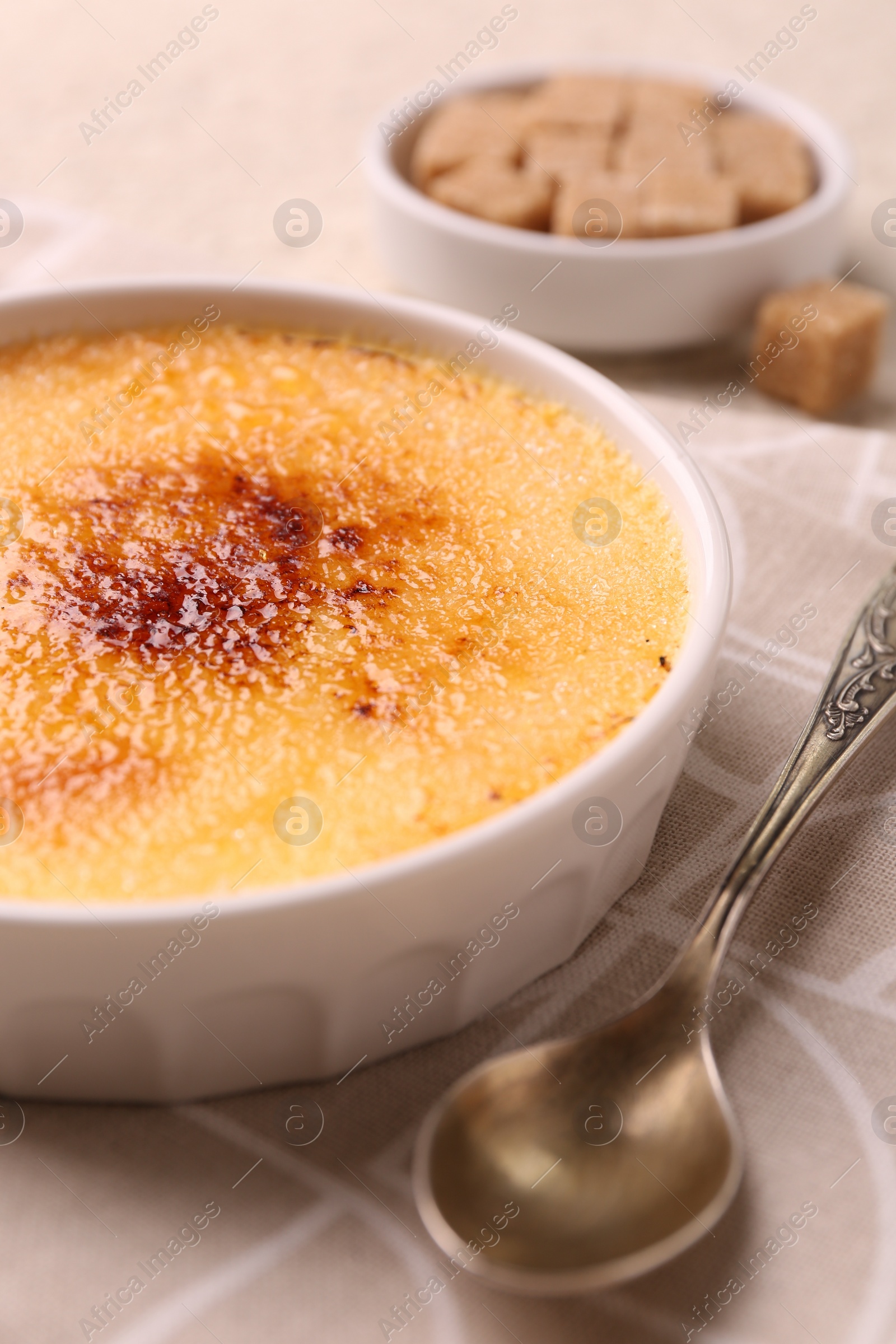 Photo of Delicious creme brulee in bowl and spoon on table, closeup