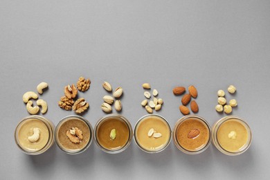 Tasty nut butters in jars and raw nuts on gray table, flat lay. Space for text