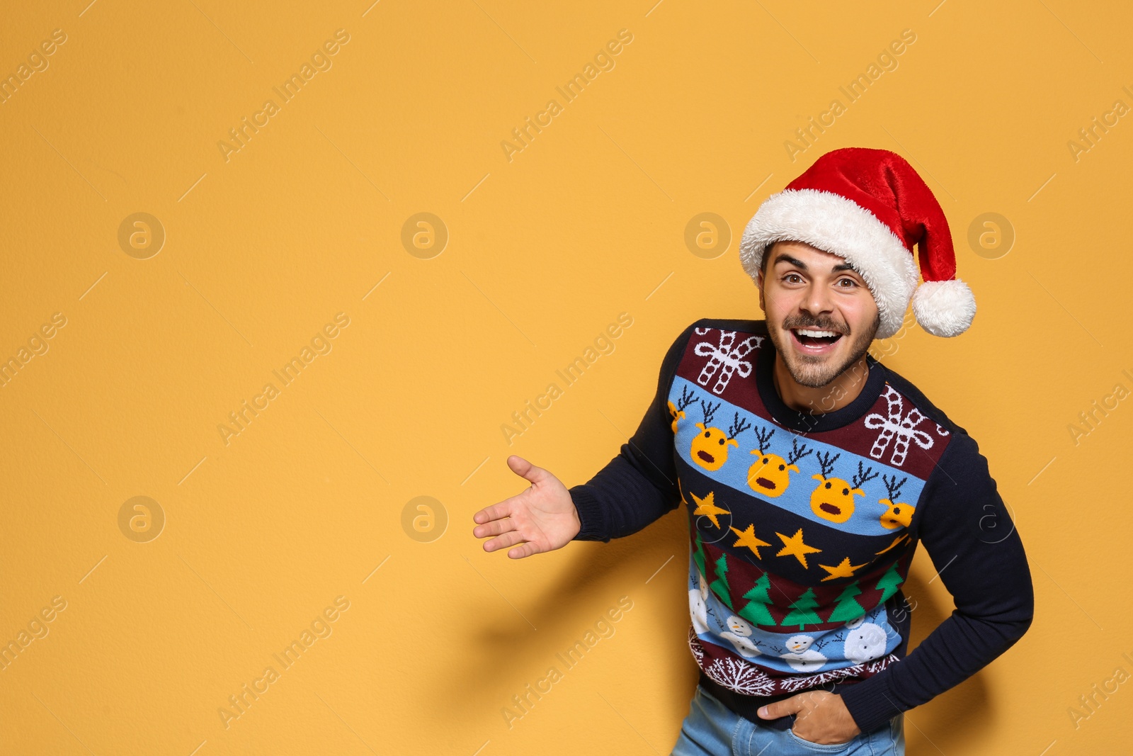 Photo of Young man in Christmas sweater and hat on color background. Space for text