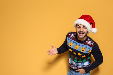 Young man in Christmas sweater and hat on color background. Space for text