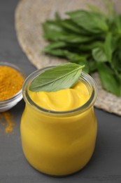 Tasty curry sauce, powder and basil leaves on grey table