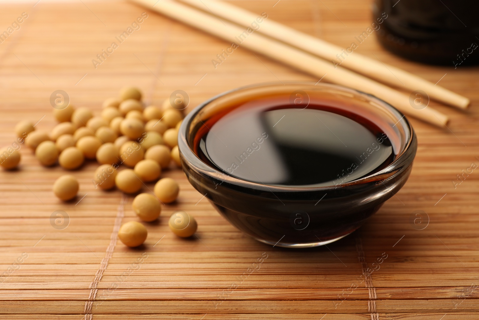 Photo of Soy sauce in bowl and soybeans on bamboo mat, closeup