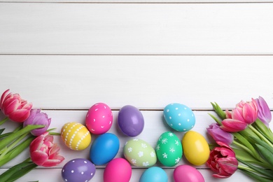 Photo of Colorful eggs and tulips on white wooden background, flat lay with space for text. Happy Easter