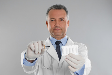 Photo of Doctor holding suppositories for hemorrhoid treatment on light grey background