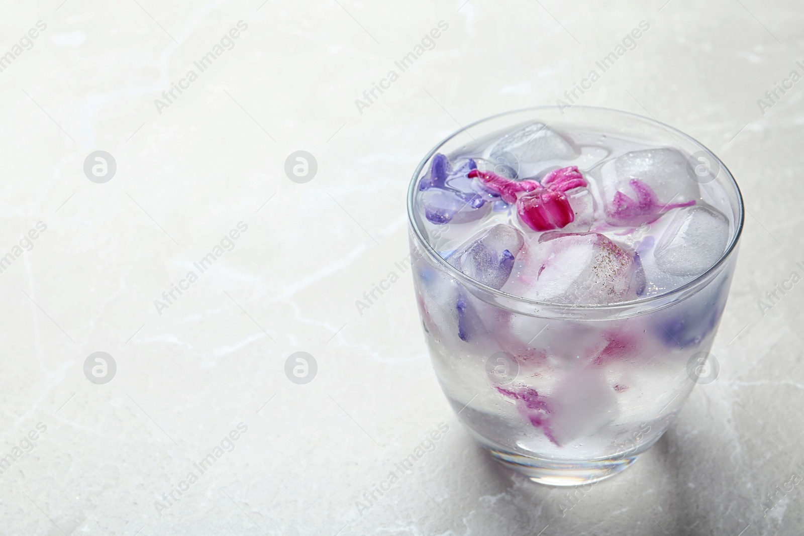 Photo of Glass of water with floral ice cubes on table. Space for text