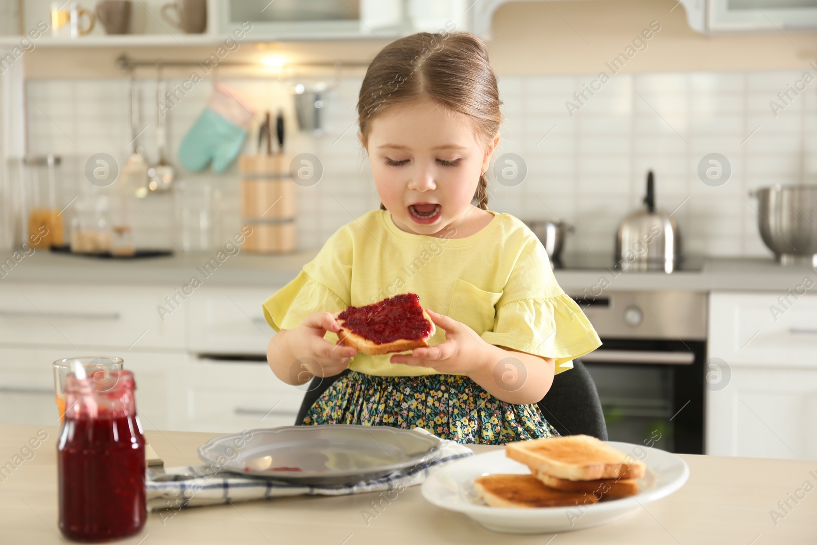 Photo of Little girl having toast with jam for breakfast in kitchen