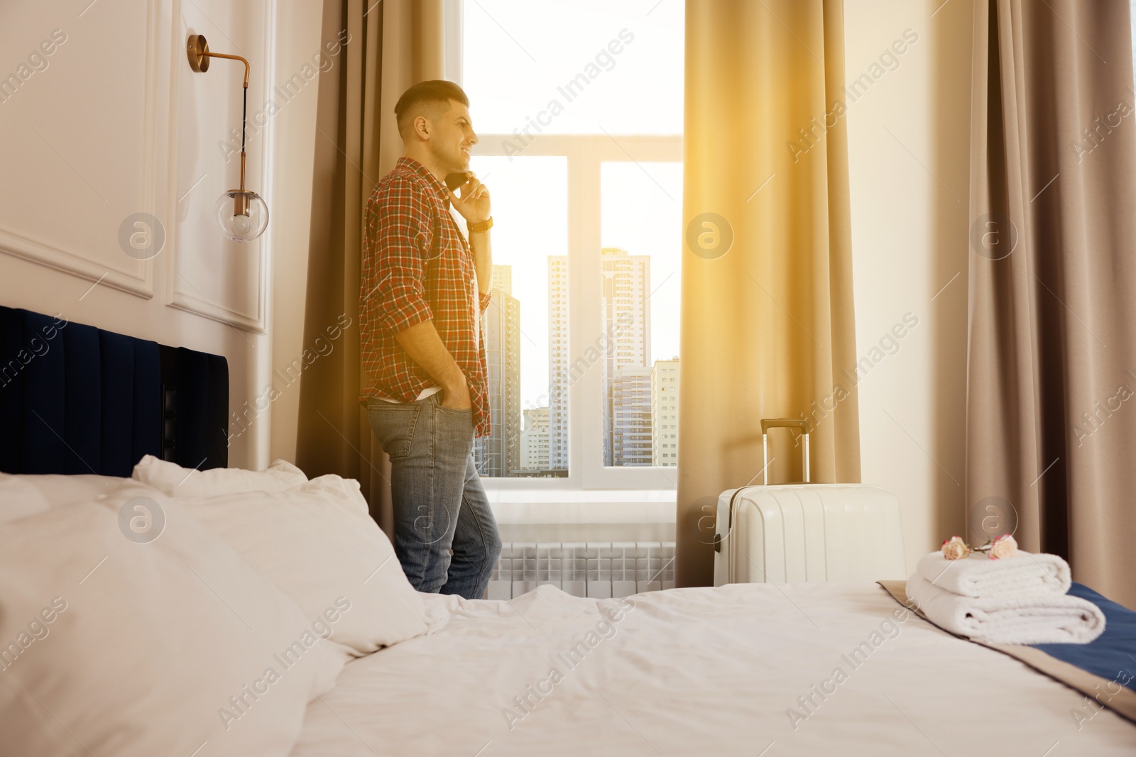 Image of Handsome man talking on phone near window in hotel room