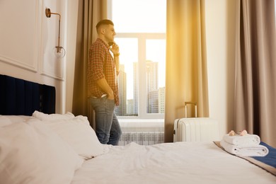Image of Handsome man talking on phone near window in hotel room