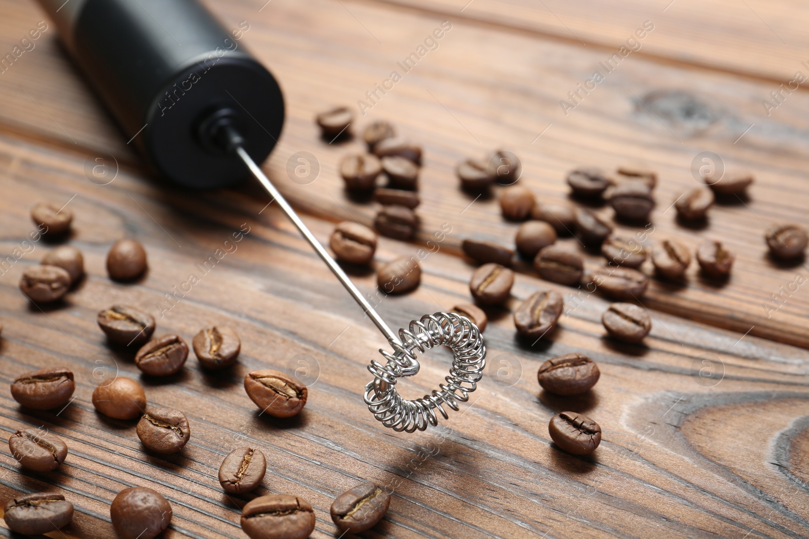 Photo of Black milk frother wand and coffee beans on wooden table, closeup