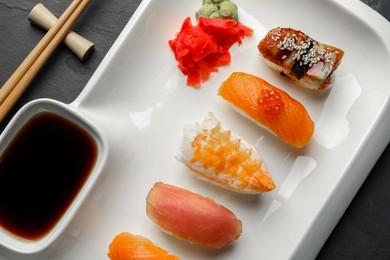 Plate with delicious nigiri sushi and soy sauce on black table, top view