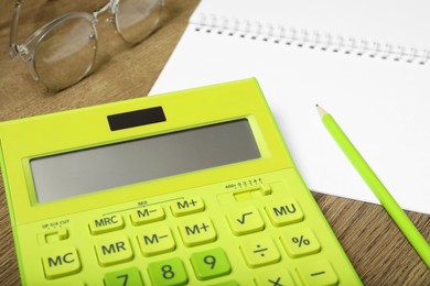 Photo of Calculator, notebook, pencil and glasses on wooden table, closeup. Tax accounting