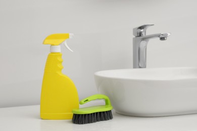 Photo of Spray bottle of cleaning product and brush near washbasin