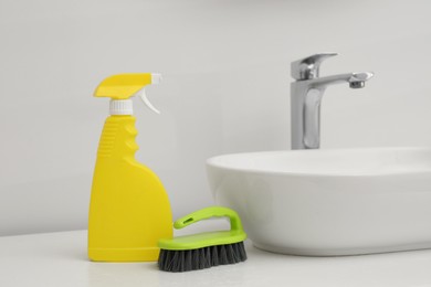 Spray bottle of cleaning product and brush near washbasin