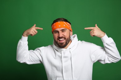Fashionable young man in stylish outfit with bandana on green background