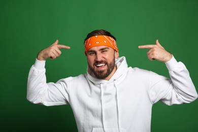 Photo of Fashionable young man in stylish outfit with bandana on green background