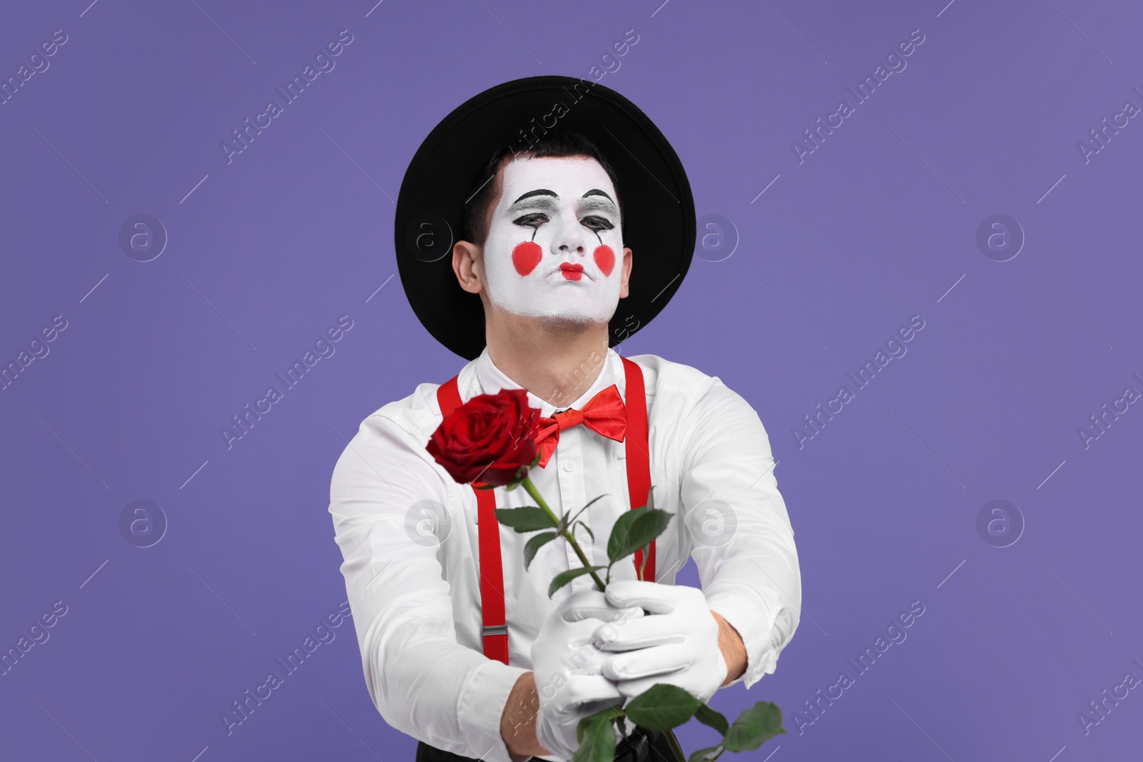 Photo of Funny mime artist with red rose on purple background