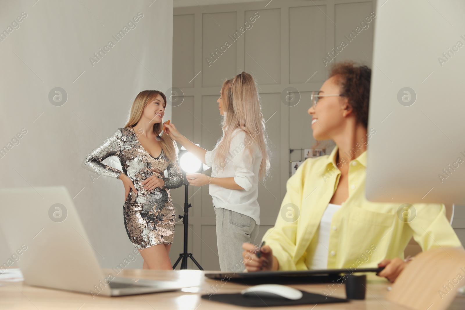 Photo of Makeup artist working with model while professional African American retoucher editing image on graphic tablet at desk in photo studio