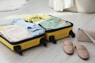 Photo of Open suitcase packed for trip, handbag and shoes on floor indoors