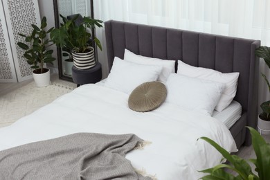 Large comfortable bed and beautiful houseplants in room. Bedroom interior