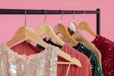 Rack with stylish women's clothes on wooden hangers against pink background, closeup