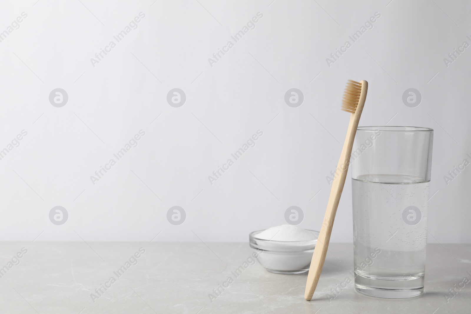 Photo of Bamboo toothbrush, bowl of baking soda and glass of water on light grey marble table. Space for text