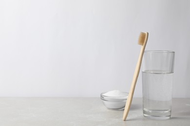 Photo of Bamboo toothbrush, bowl of baking soda and glass of water on light grey marble table. Space for text