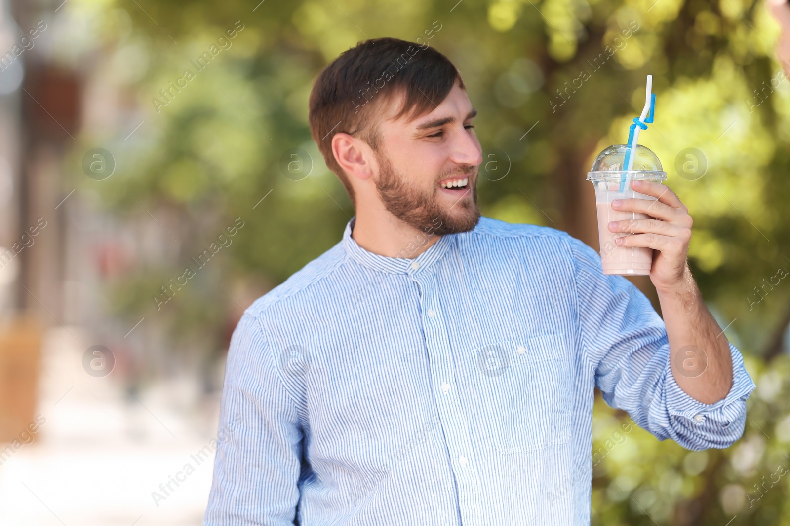 Photo of Young man with cup of delicious milk shake outdoors