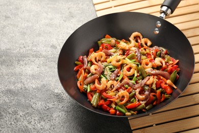 Photo of Shrimp stir fry with vegetables in wok on grey table