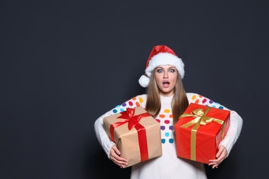 Photo of Emotional young woman with Christmas gifts on dark background. Space for text
