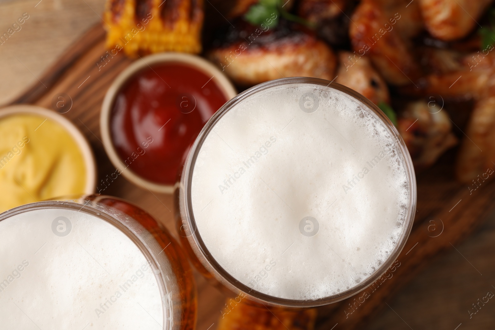 Photo of Glasses with beer, delicious baked chicken wings and grilled corn on table, closeup