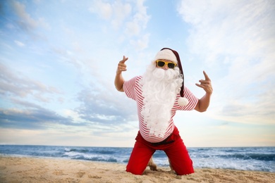 Photo of Santa Claus having fun on beach, space for text. Christmas vacation