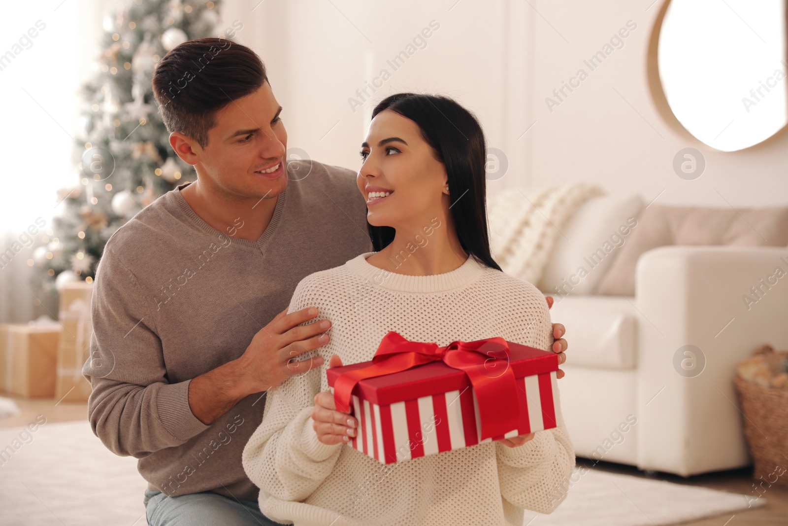 Photo of Boyfriend giving Christmas gift box to his girlfriend in living room