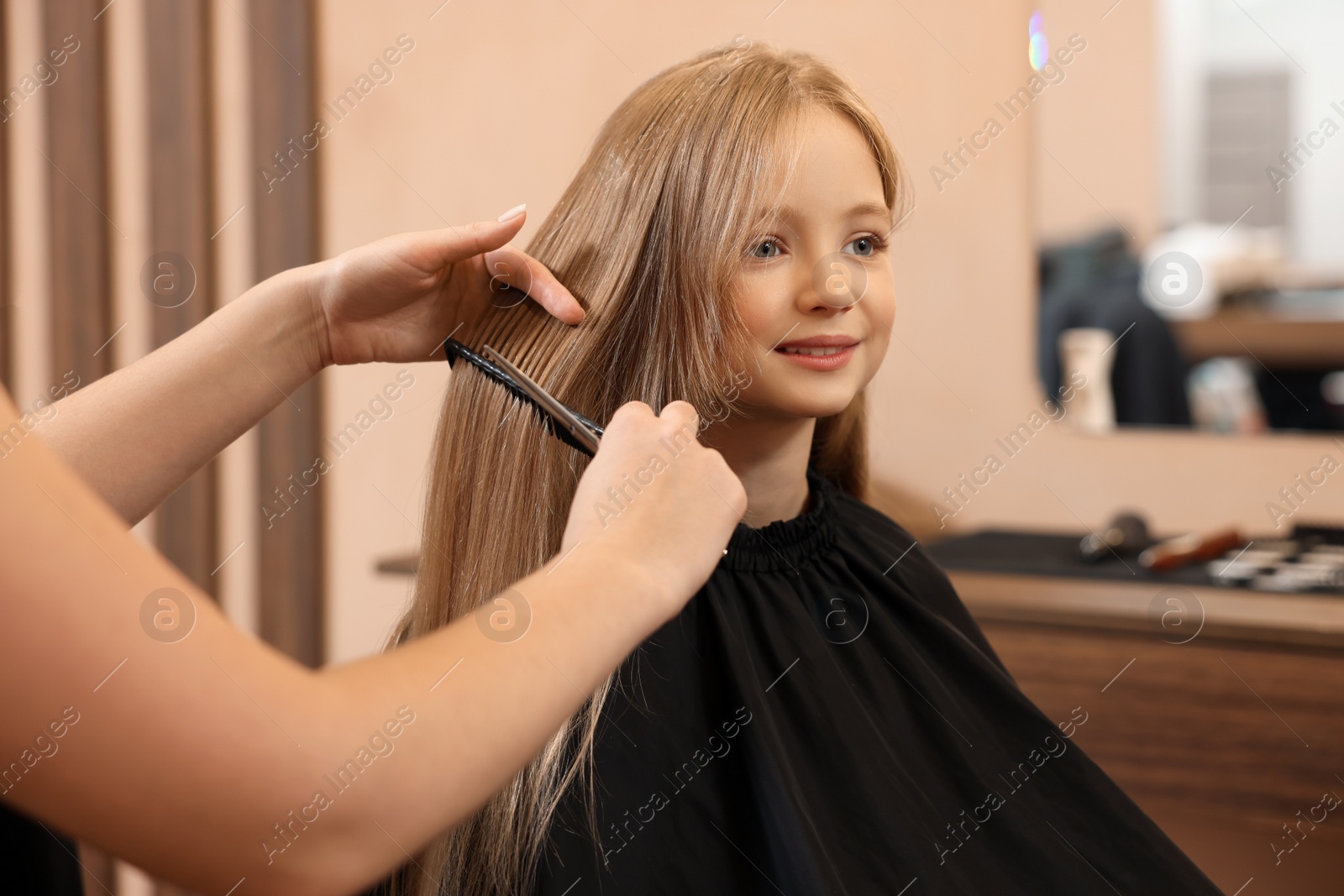 Photo of Professional hairdresser combing girl's hair in beauty salon